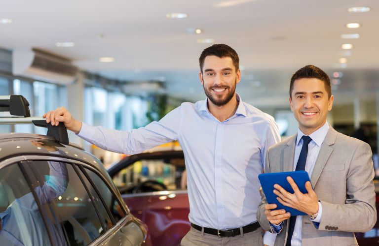 Buyer and sales representative standing side-by-side after a used car inspection and sale